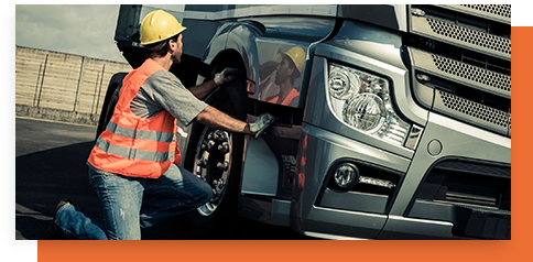 A man in an orange vest and hard hat working on a truck.